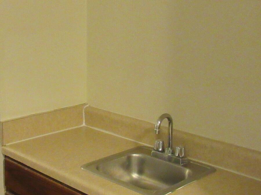 A kitchen with a stainless steel sink, beige countertop, and wooden cabinets.