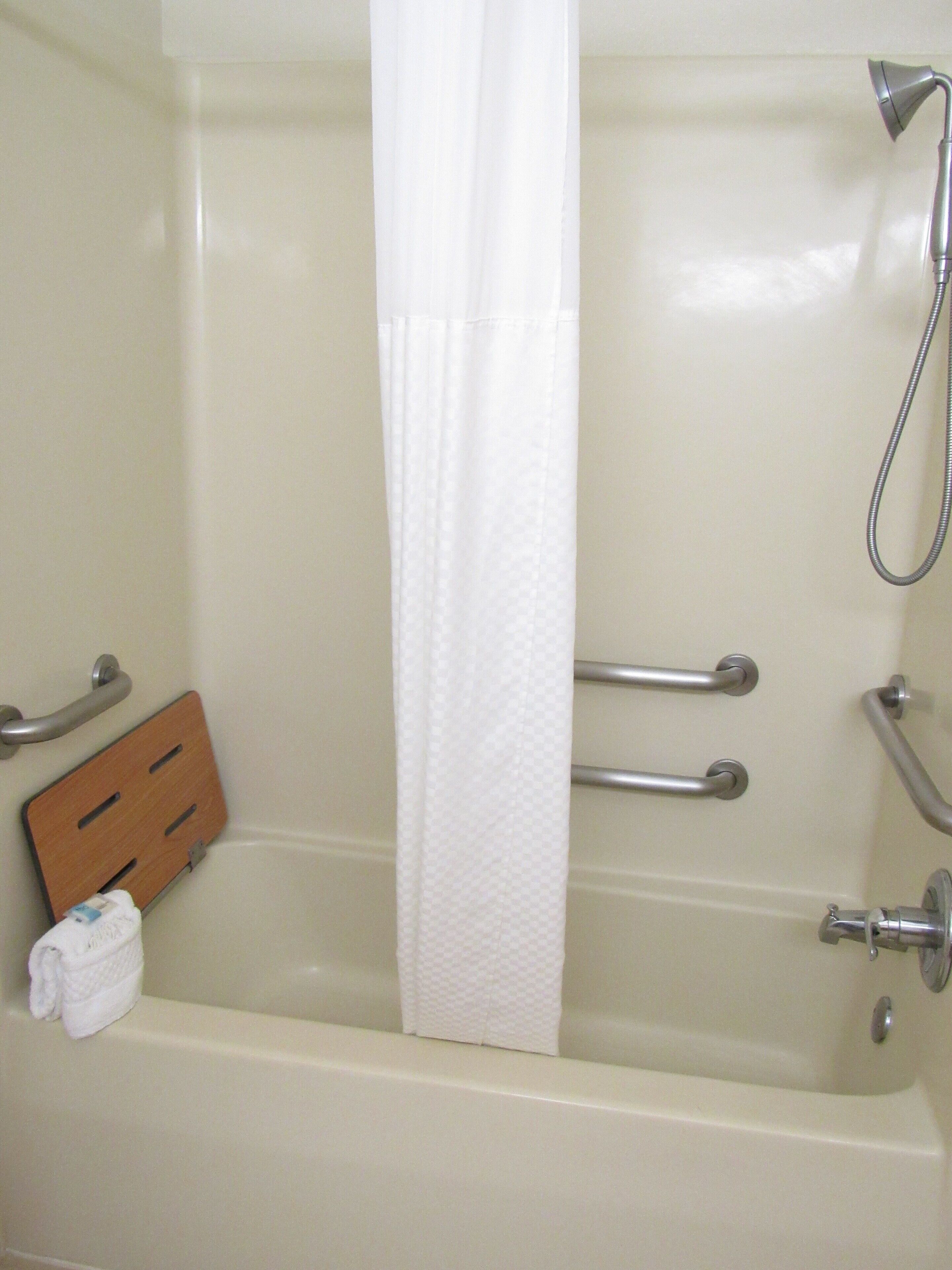 A bathtub with a shower head, grab bars, and a towel rack.