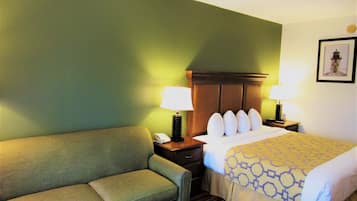 A hotel room with a green wall, a bed with a patterned bedspread, a green sofa, two bedside tables with lamps, and a framed picture on the wall.