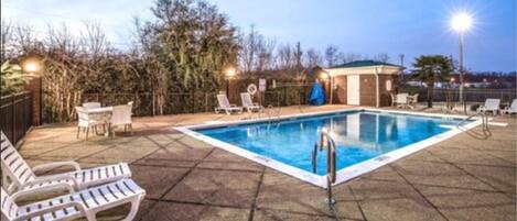 A rectangular swimming pool with a metal ladder, surrounded by lounge chairs and a covered seating area.