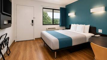 A hotel room with a bed, a desk, a chair, a TV, and a window with a view of trees.
