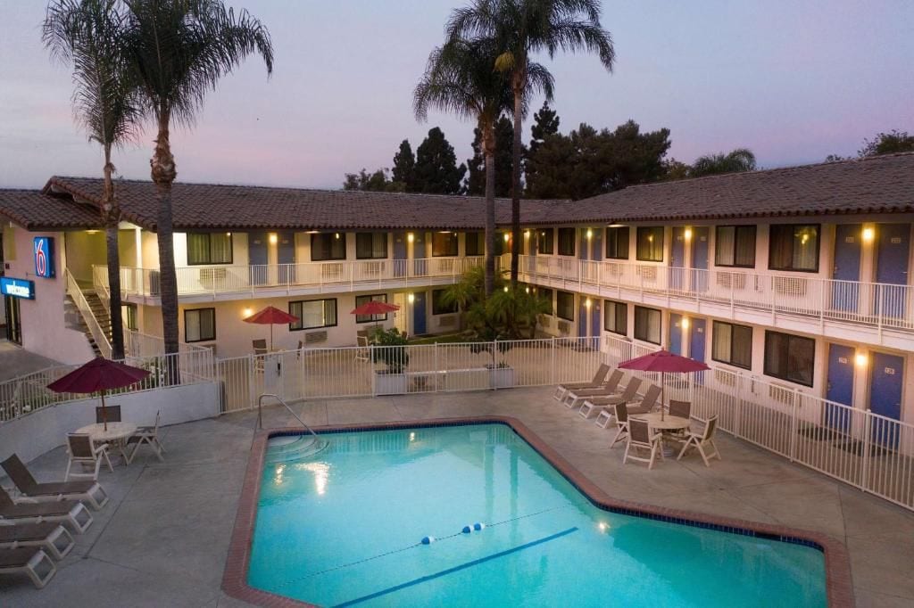 Un motel con piscina, mobiliario exterior y un edificio de dos pisos con balcones.