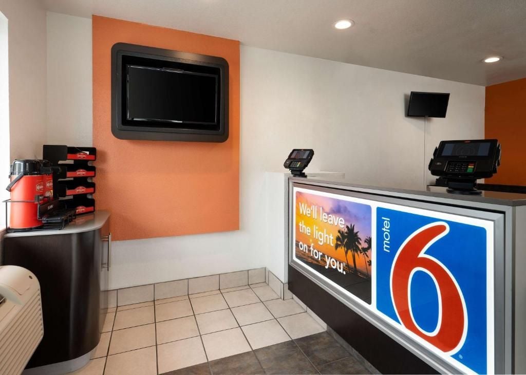 A reception area with a digital display, a television, and a counter with a sign.