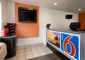 Un área de recepción con pantalla digital, televisión y mostrador con un cartel.