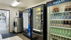 A row of vending machines with various beverages and snacks, a refrigerator, and a water dispenser. - Vagabond Inn Camarillo (Camarillo)