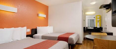 A hotel room with two beds, a wooden dining table, a mirror, and a kitchenette.