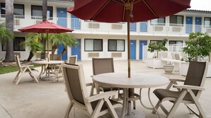 A hotel courtyard with outdoor seating, including tables and chairs, and red umbrellas. - Vagabond Inn Camarillo (Camarillo)