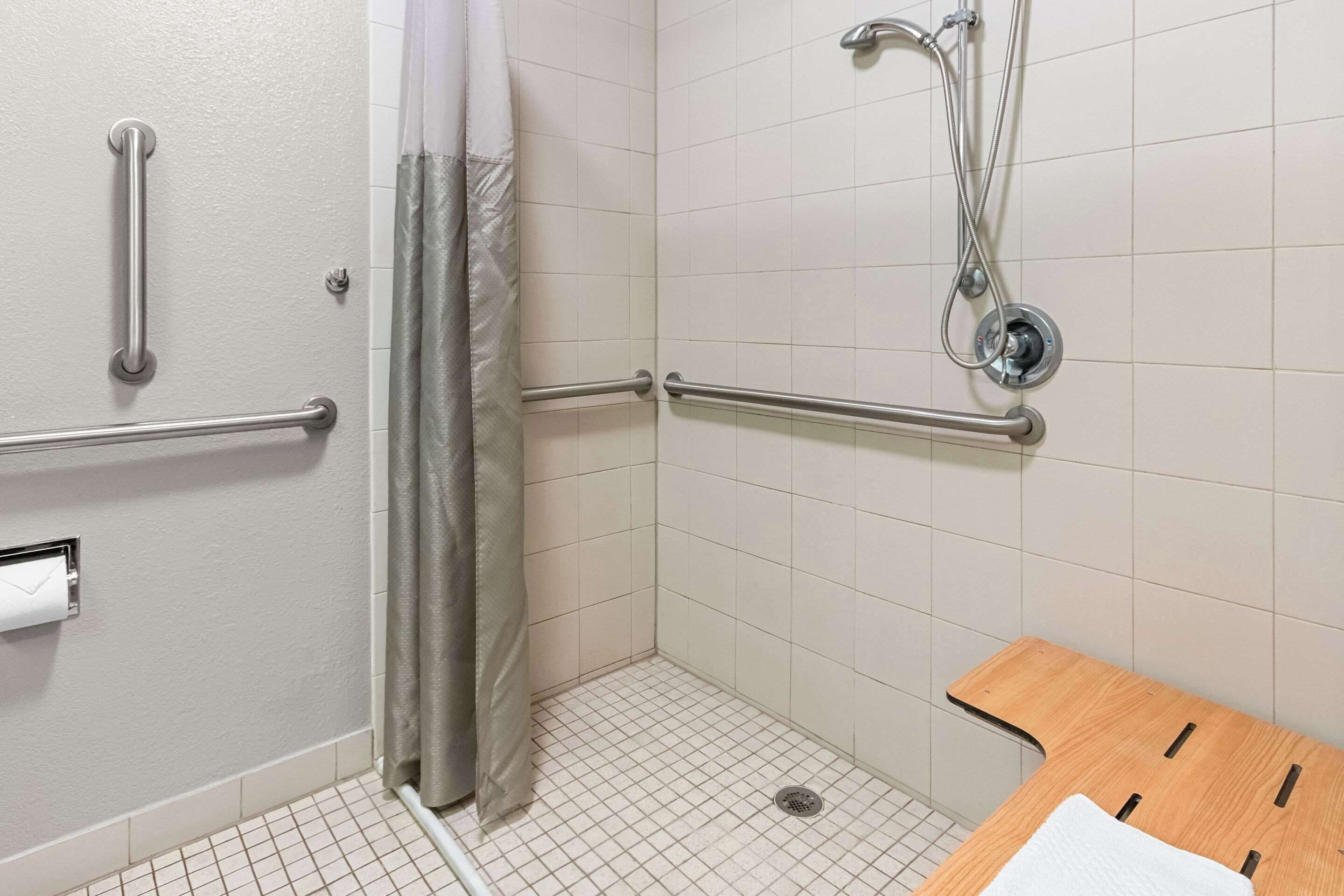 Un baño con paredes de azulejos blancos, una ducha con cortina y un banco de madera.