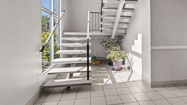Una escalera moderna con barandilla de vidrio que lleva a un rellano con una planta en maceta.