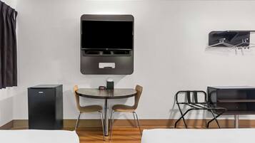 A compact hotel room with a bed, a desk, a chair, a small table, and a TV mounted on the wall.