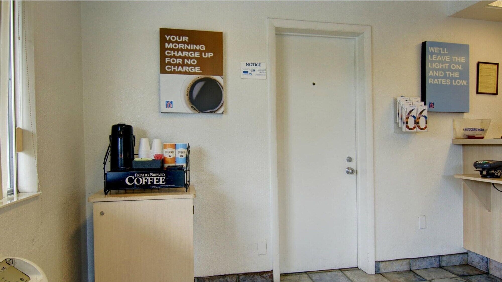 A small room with a coffee station, a door, and a wall-mounted sign.