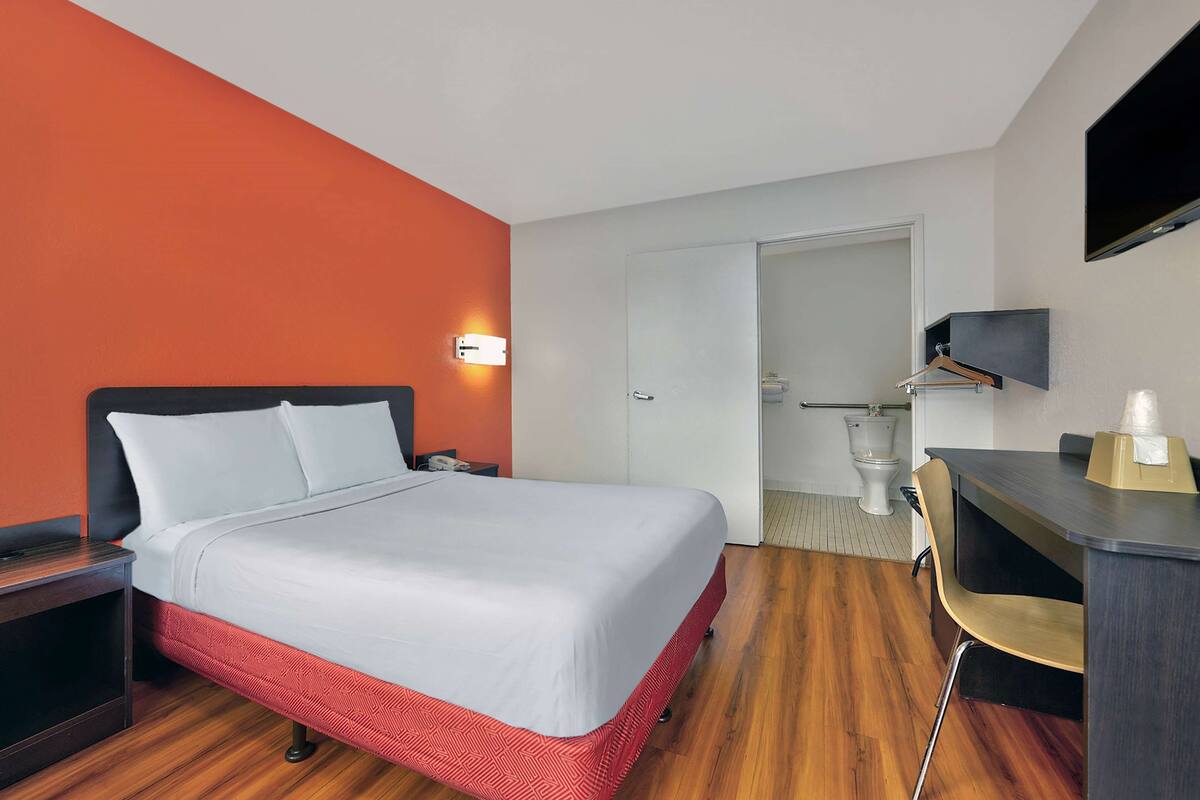 A hotel room with a bed, a desk, a chair, a TV, and a bathroom.