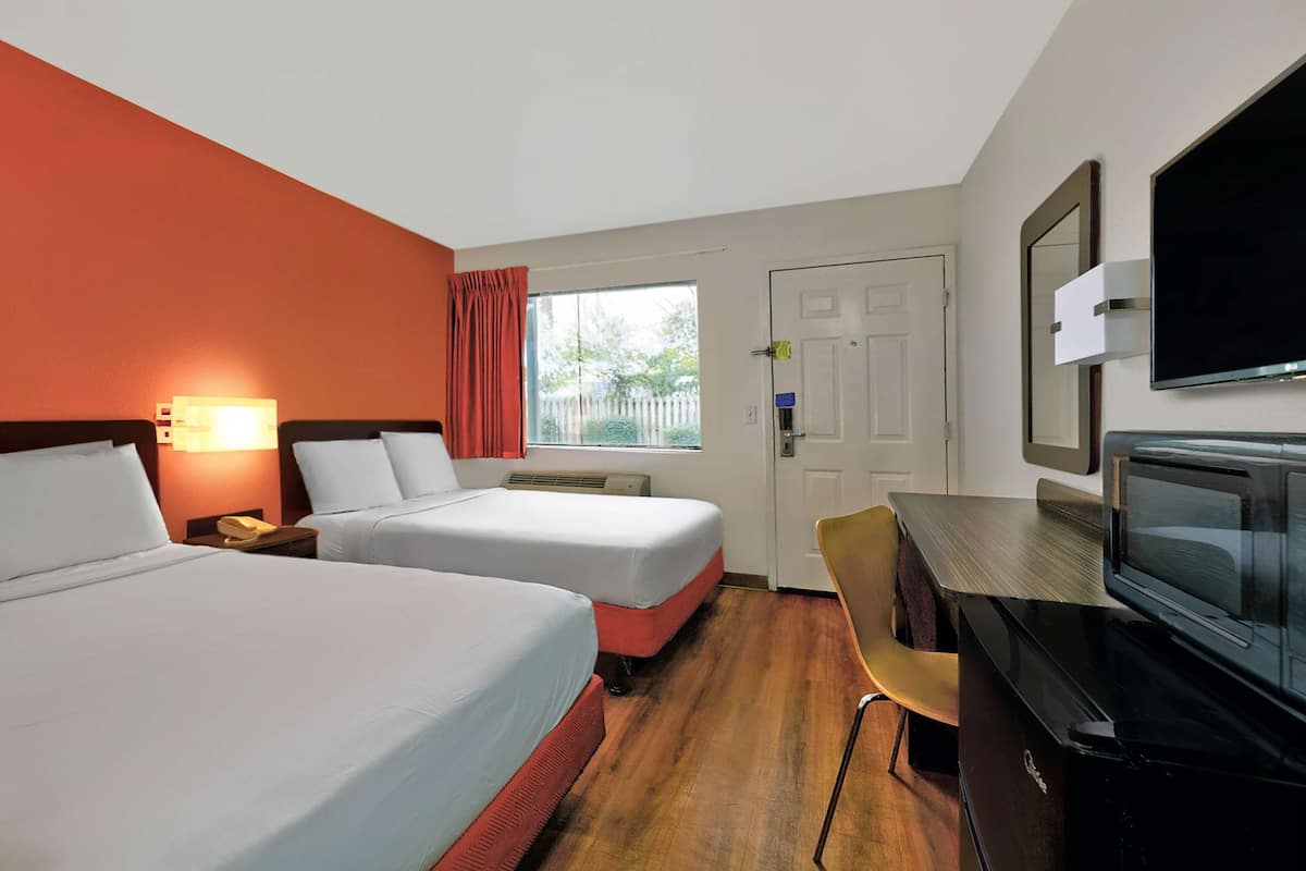 A hotel room with two beds, a desk with a television, a chair, and a window with curtains.