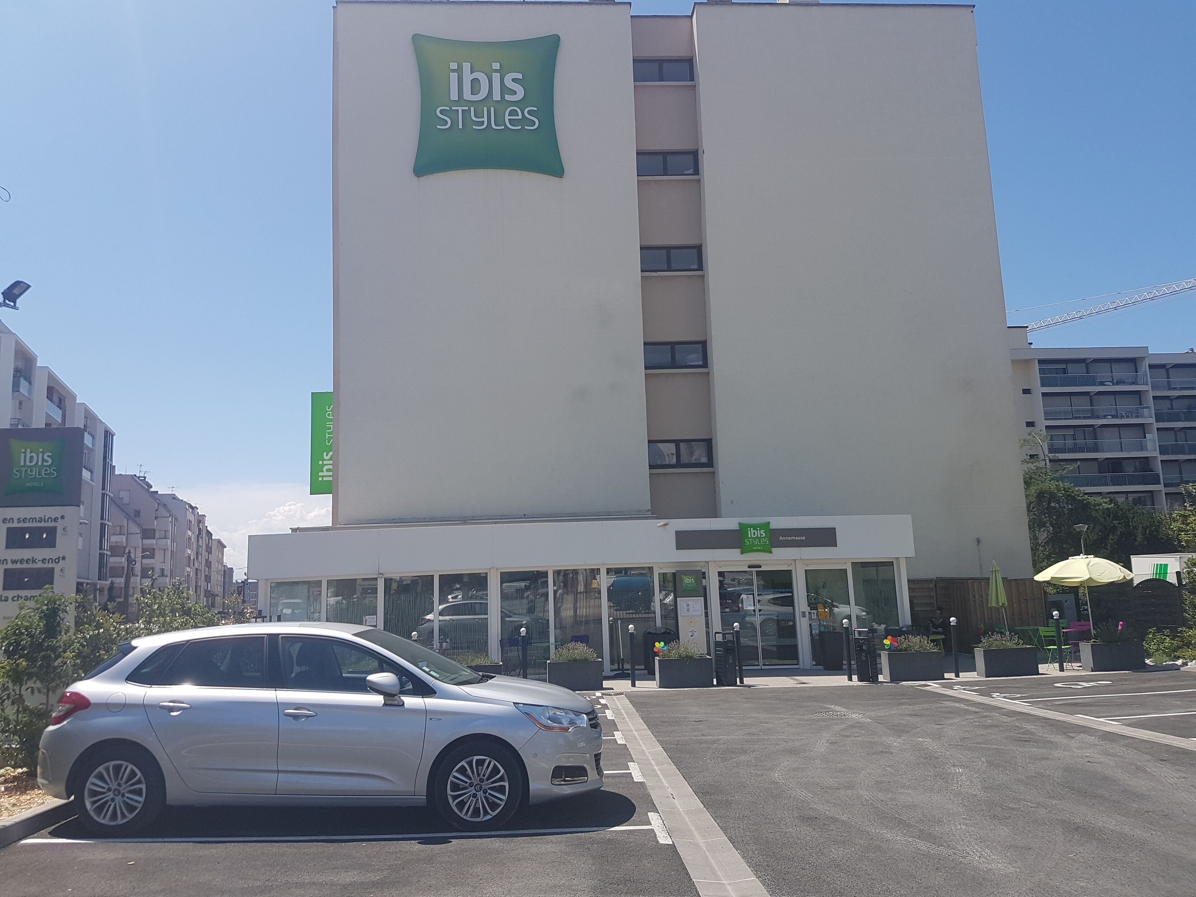 A building with 'ibis Styles' signage, featuring a modern design with a prominent entrance and a parking area in front.