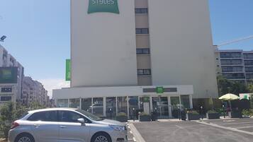 A building with 'ibis Styles' signage, featuring a modern design with a prominent entrance and a parking area in front.