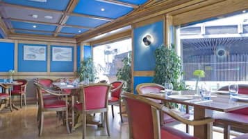 Un restaurante con mesas de madera, sillas rojas, ventanas amplias y paredes azules.