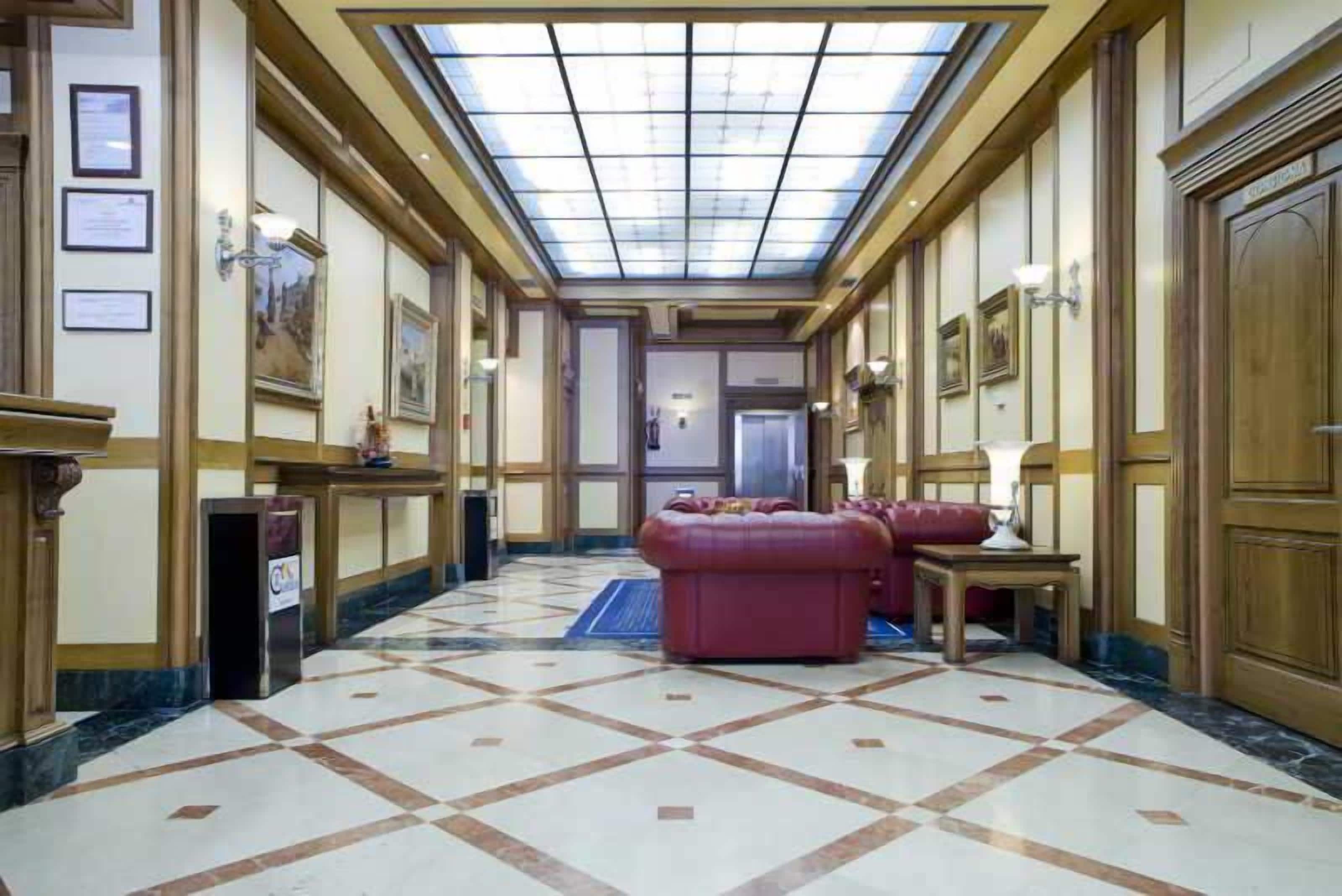 Un vestíbulo de hotel con techo alto, una zona de estar central y un suelo estampado.