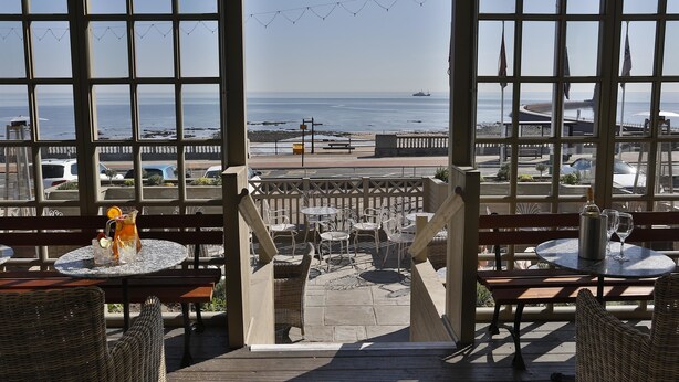 A terrace with wicker furniture, a table with a bottle and glasses, and a view of the sea and beach. - The Roker Hotel, BW Premier Collection (Sunderland)