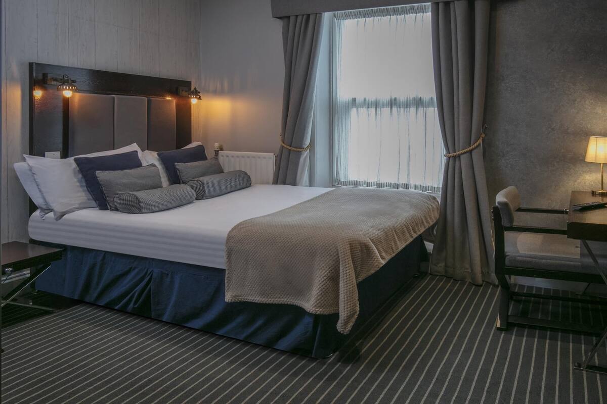 A neatly arranged hotel room with a bed, bedside table, lamp, and a view of the outdoors.