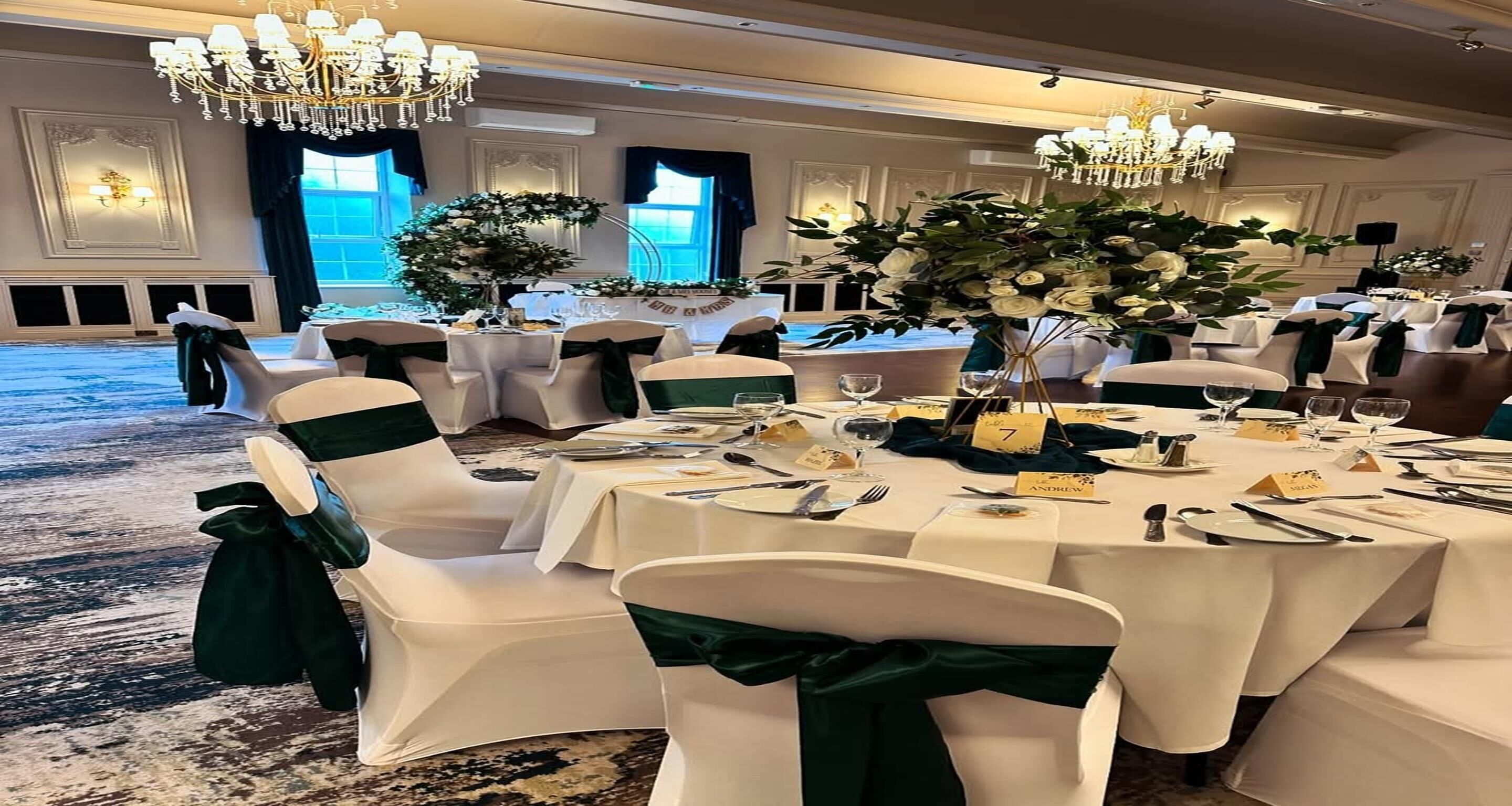 Un salón de banquetes con mesas redondas, manteles blancos y cintas verdes en las sillas.
