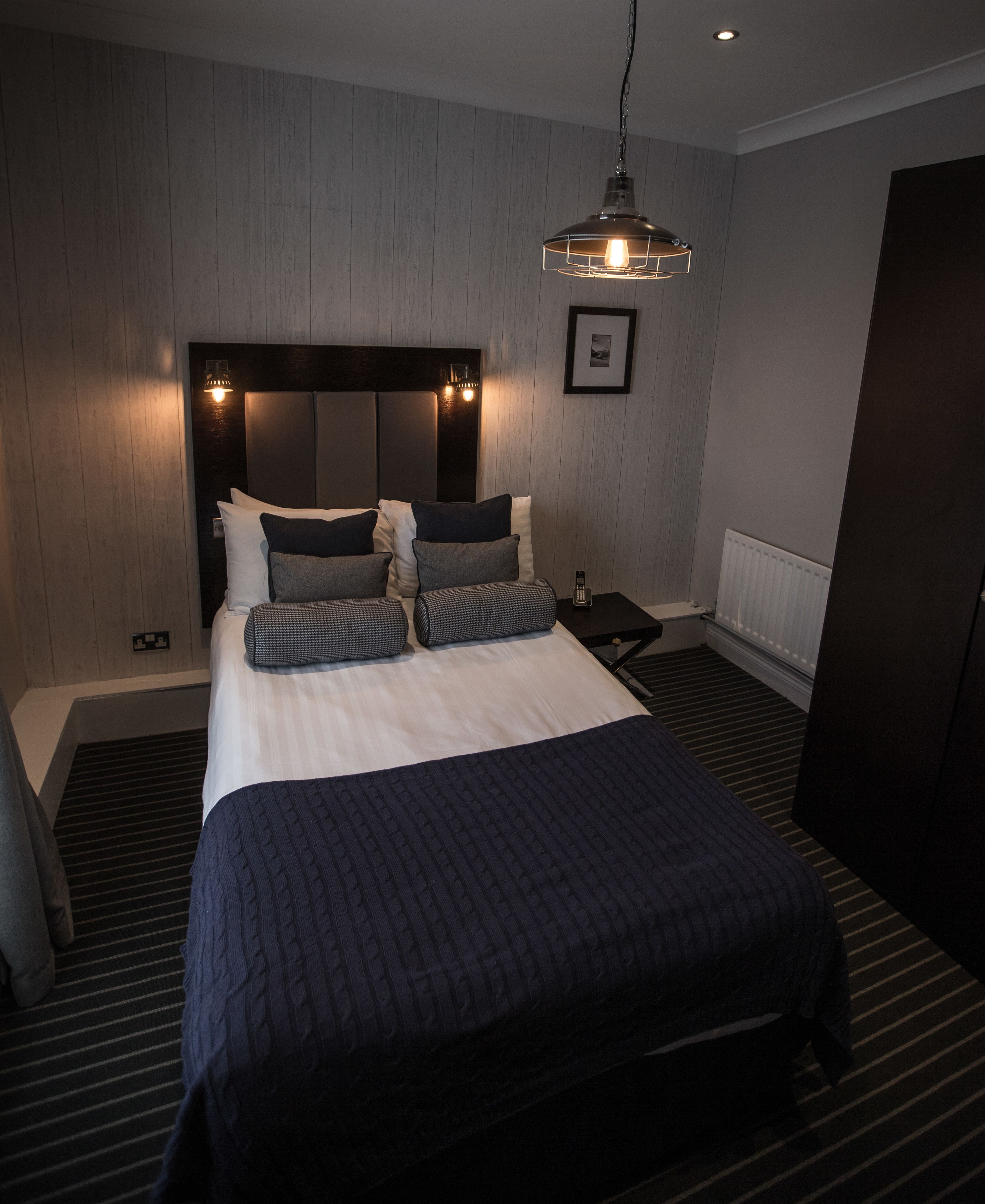 A modern hotel room with a large bed, a bedside table, a nightstand, and a hanging light fixture.