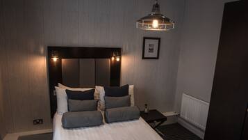A modern hotel room with a large bed, a bedside table, a nightstand, and a hanging light fixture.