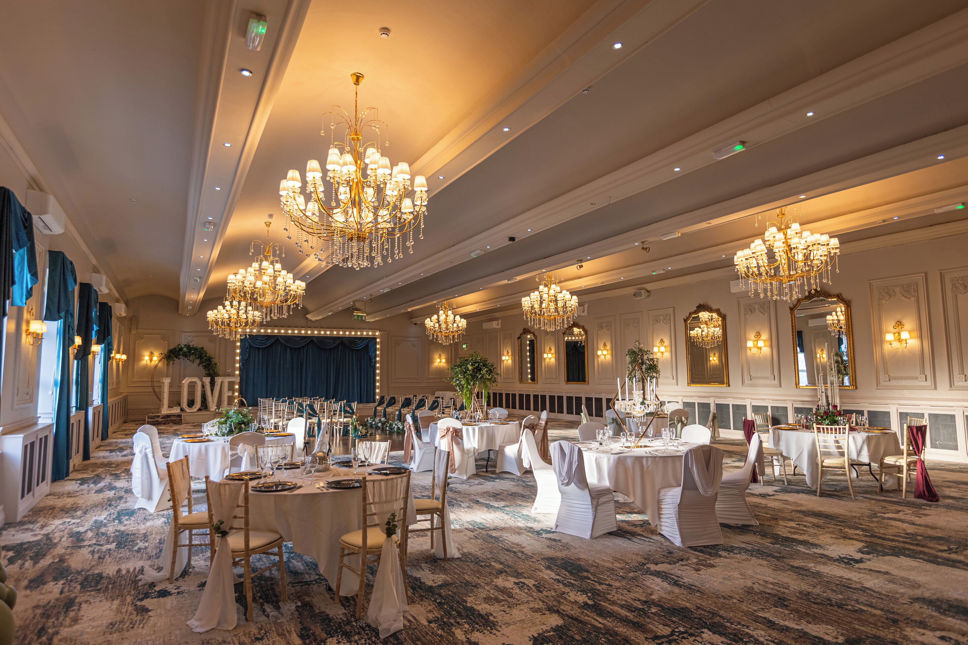 A banquet hall with multiple round tables set for a formal event, adorned with white tablecloths and chairs.
