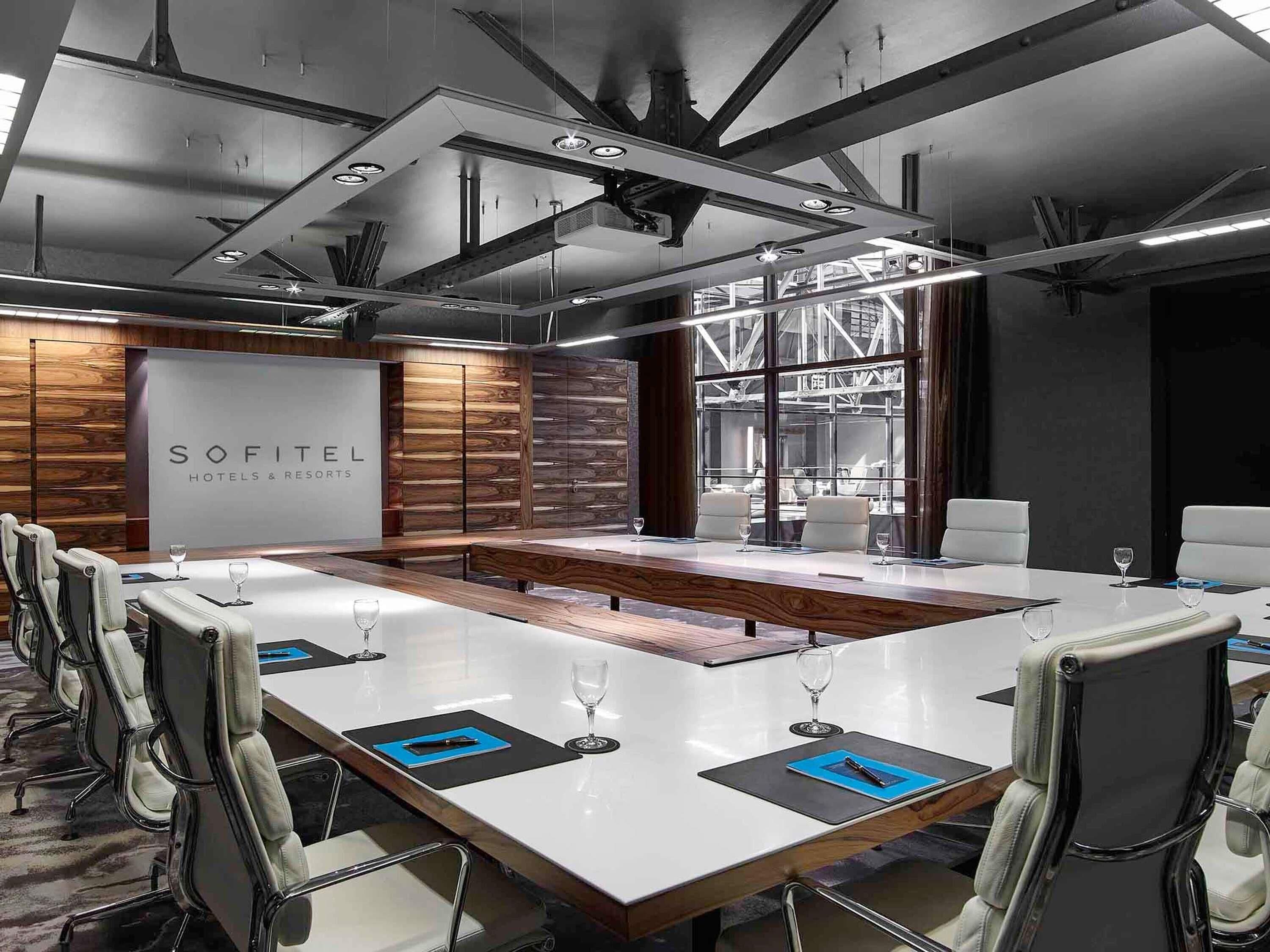 Une salle de conférence avec une longue table, des chaises blanches et une enseigne indiquant « SOFITEL HOTELS & RESORTS ».