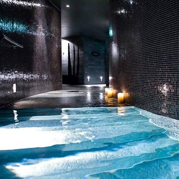 A spa area with a hot tub, tiled walls, and a wet floor.