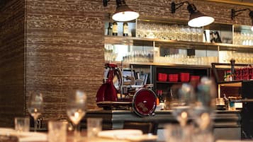 Interno di un ristorante con pareti in mattoni, tavoli, sedie e un'area bar con scaffali e bottiglie.