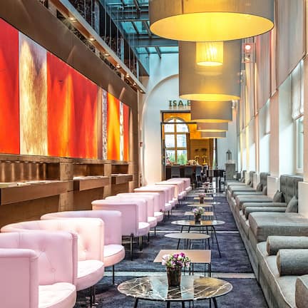 A hotel lobby with rows of seating, a large wall with abstract art, and a visible reception area.