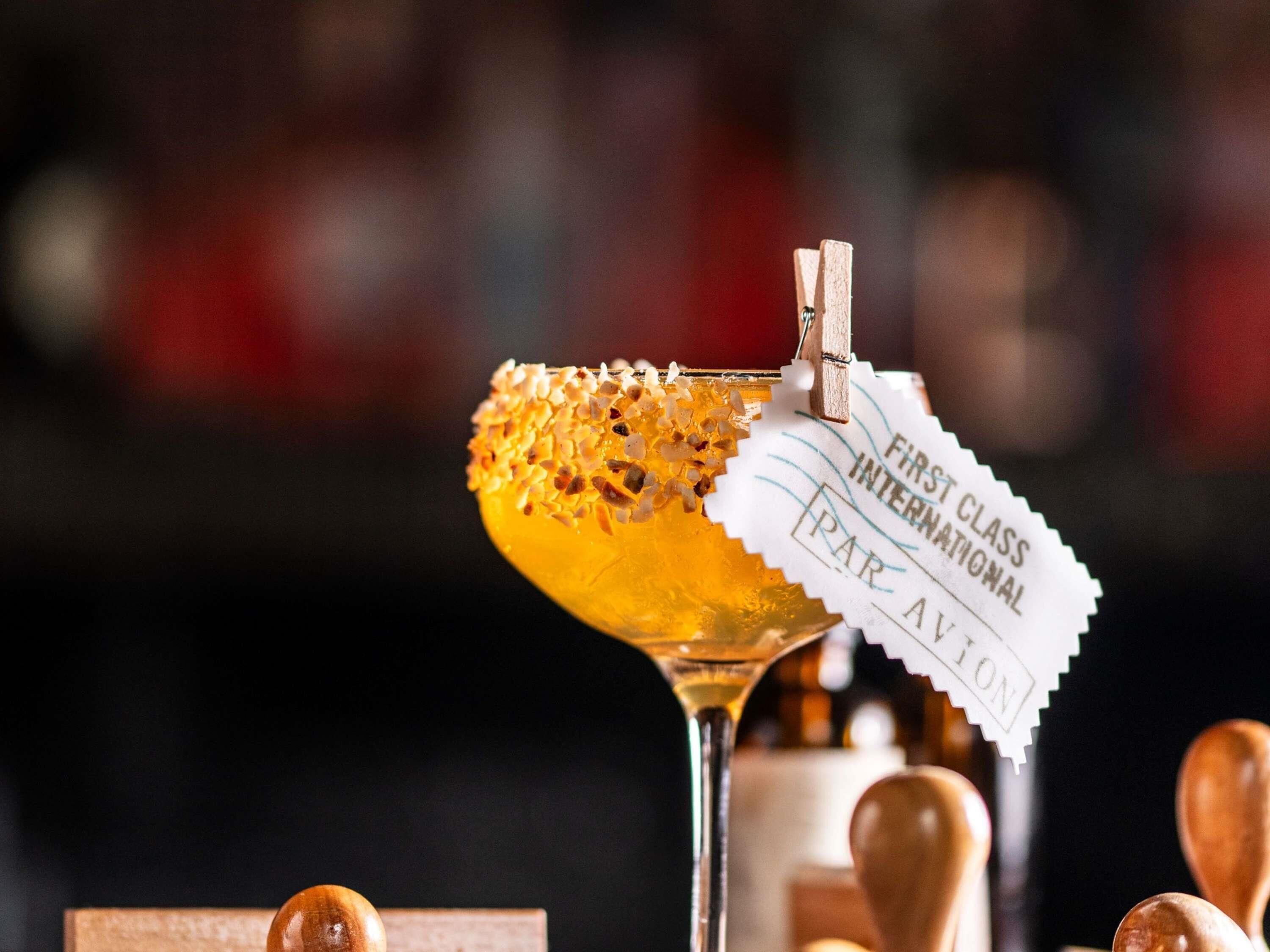 En cocktail dekorerad med en bit bikakshonung och en etikett med texten ”FÖRSTAKLASSS, INTERNATIONELL, FRATZ AVION”.