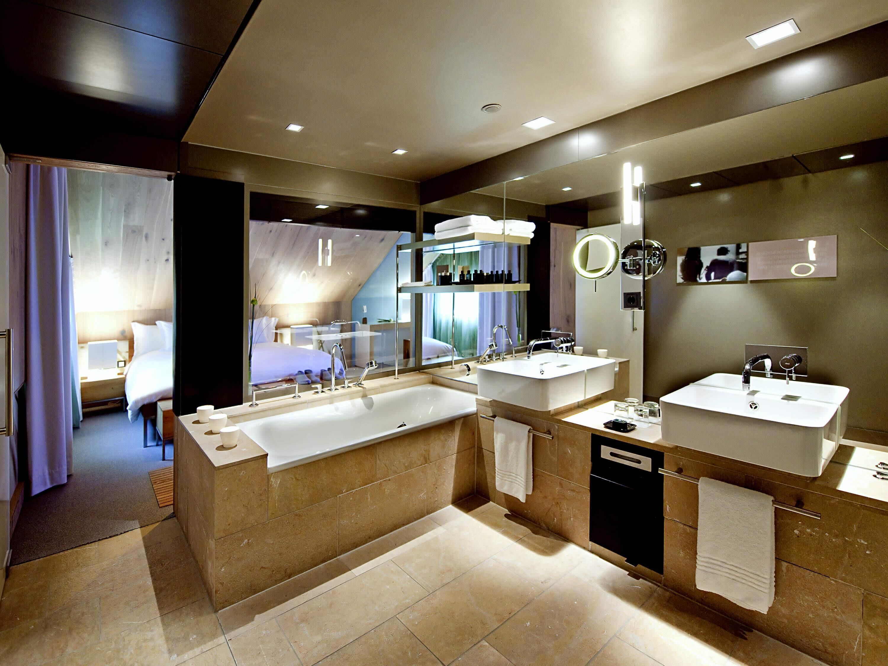 A modern bathroom with a large bathtub, two sinks, and a mirror with a round mirror above.