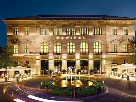 Ein Hotel mit einer zentralen Fontäne, Bogenfenstern und einem Schild mit der Aufschrift 'SOPITEL'.. Sofitel Munich Bayerpost