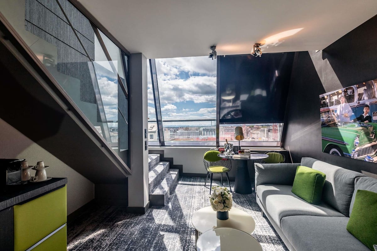 Un salon moderne avec un canapé, une table basse et une vue sur la ville grâce à de grandes fenêtres.