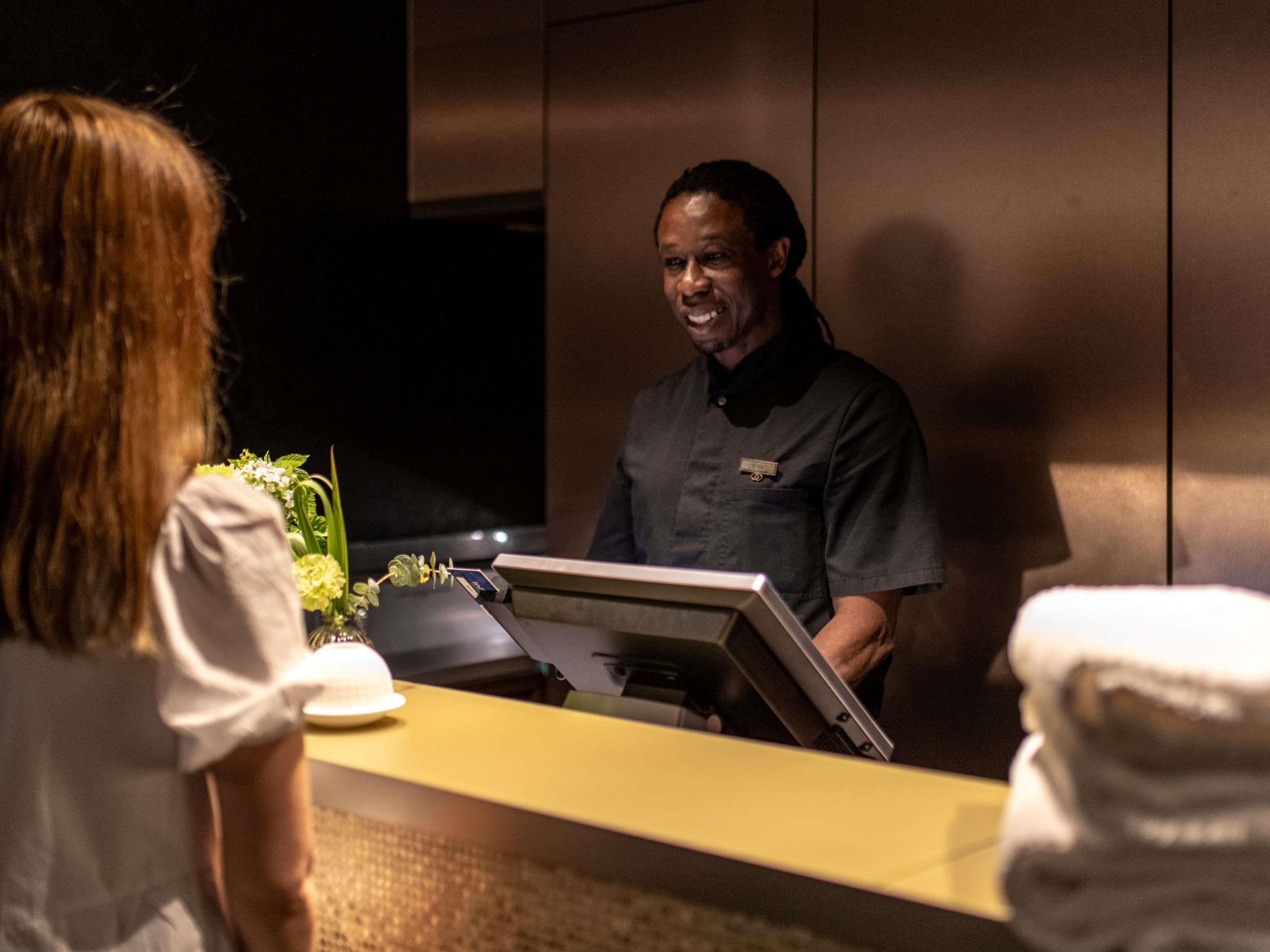 A hotel reception area with a counter, a guest, and a staff member.
