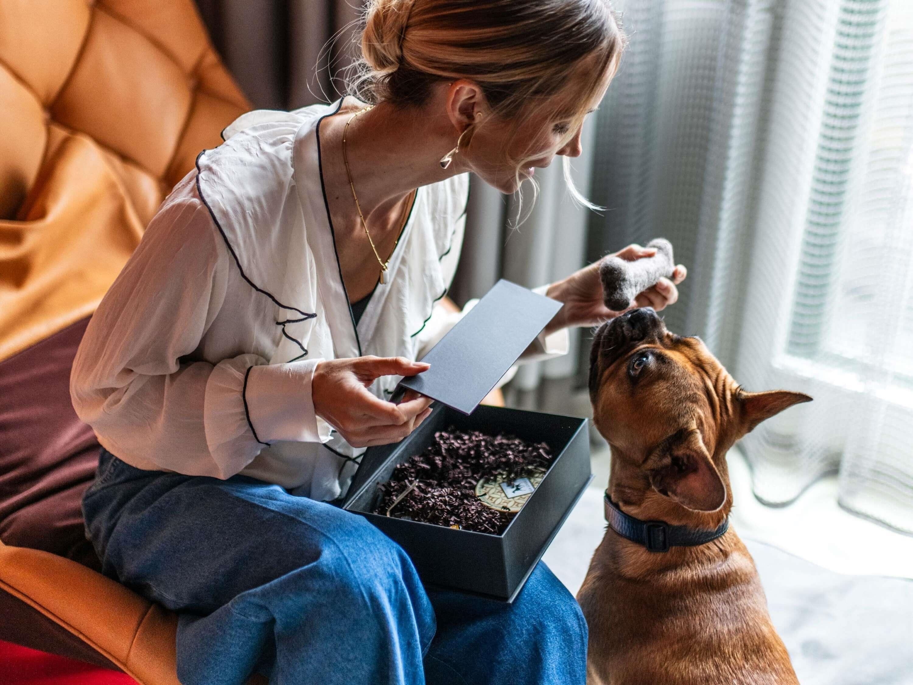Une personne assise sur un canapé, avec un chien, tenant une boîte et une feuille de papier.