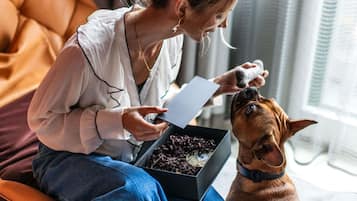 Une personne assise sur un canapé, avec un chien, tenant une boîte et une feuille de papier.