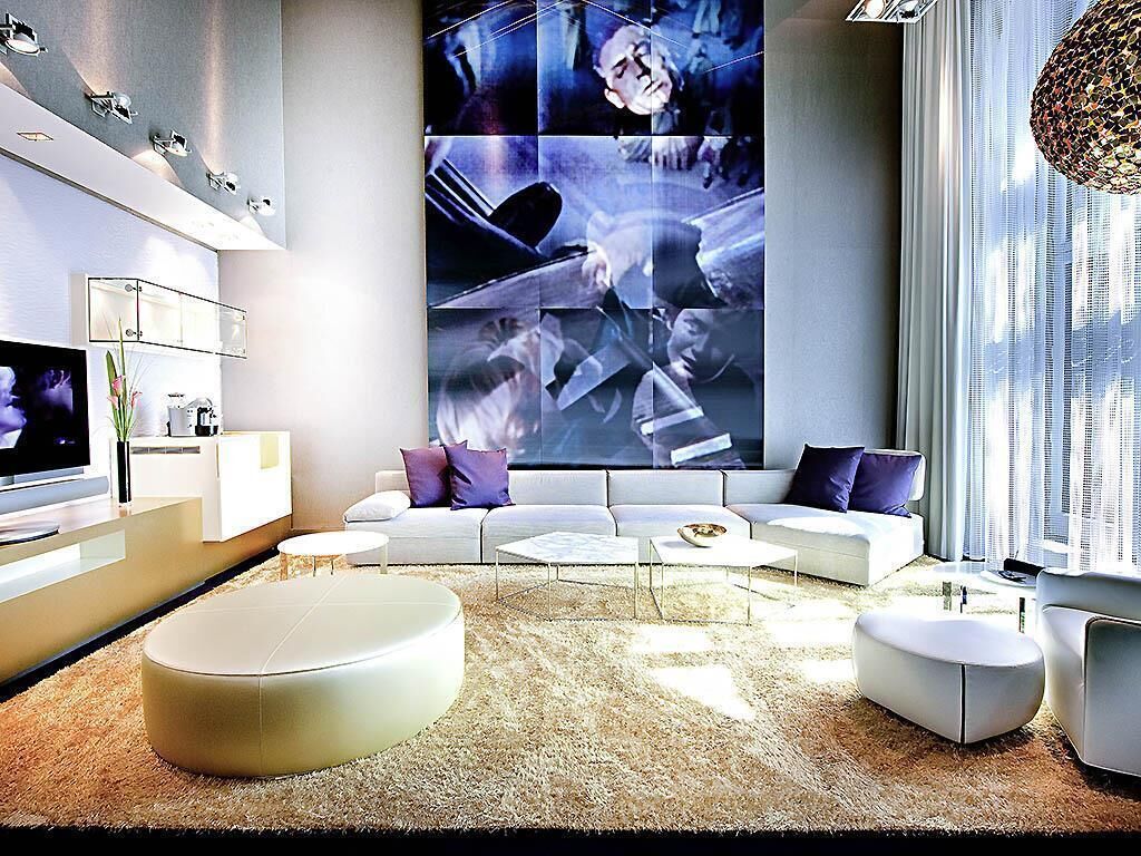Een moderne woonkamer met een grote muurschildering, een zithoek, een flatscreen televisie en een salontafel.