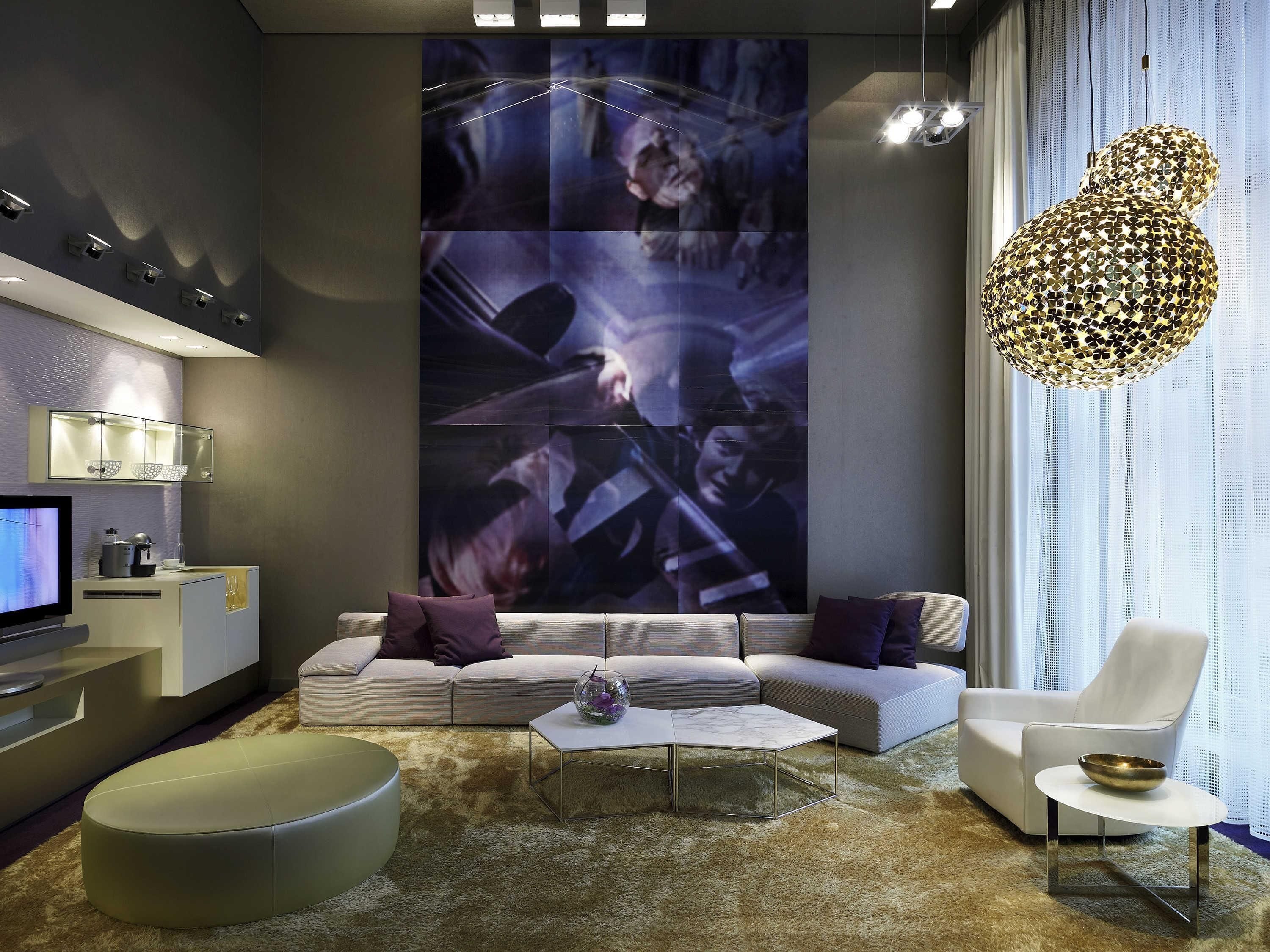 A modern living room with a large wall-mounted TV, a sofa, a coffee table, and a decorative light fixture.