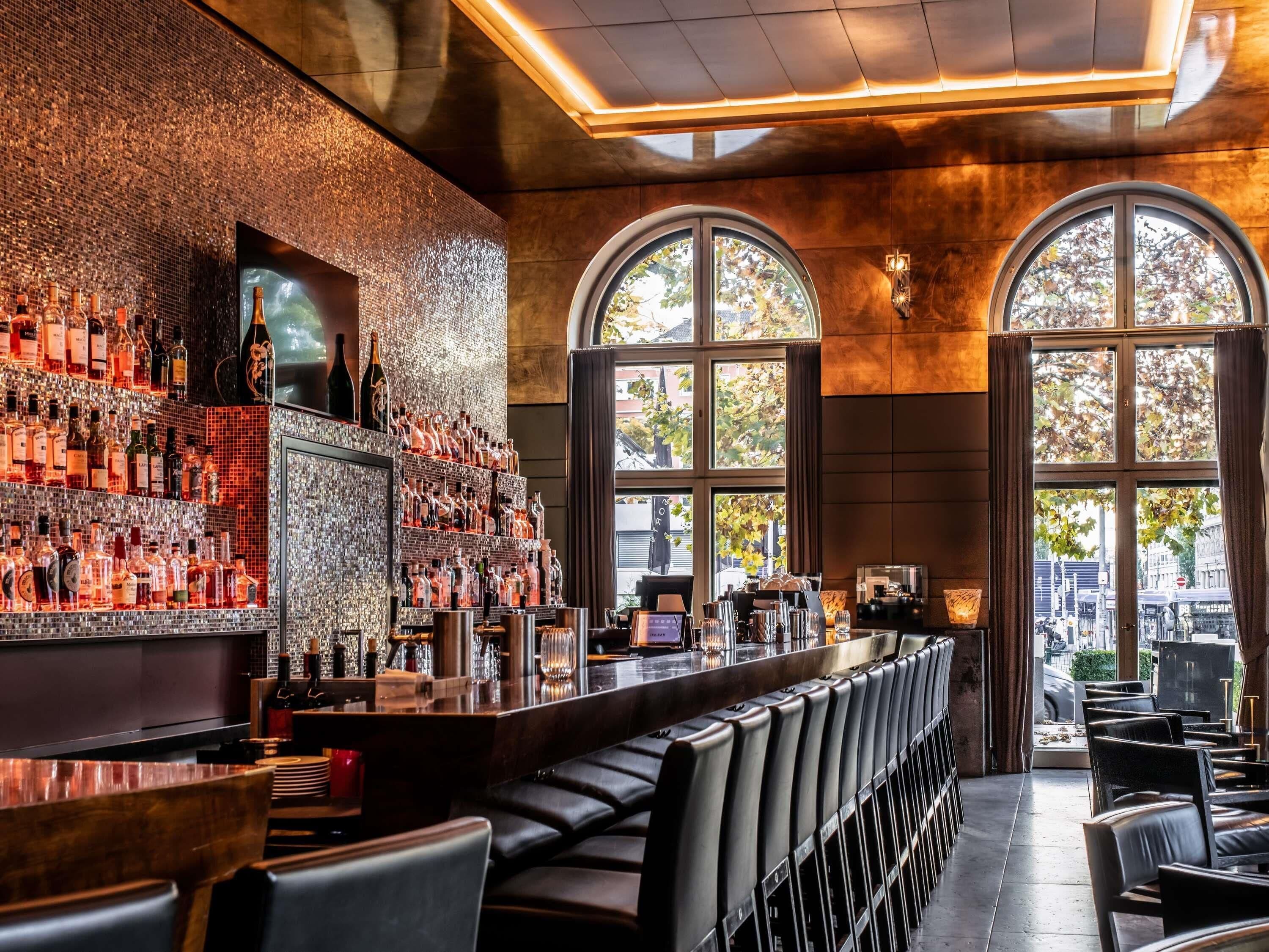 A bar with a long counter, multiple seating areas, and large arched windows.