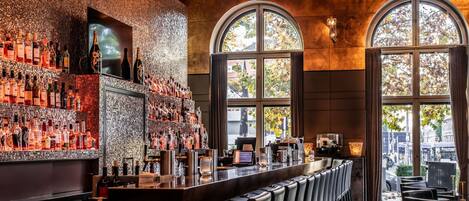 A bar with a long counter, multiple seating areas, and large arched windows.