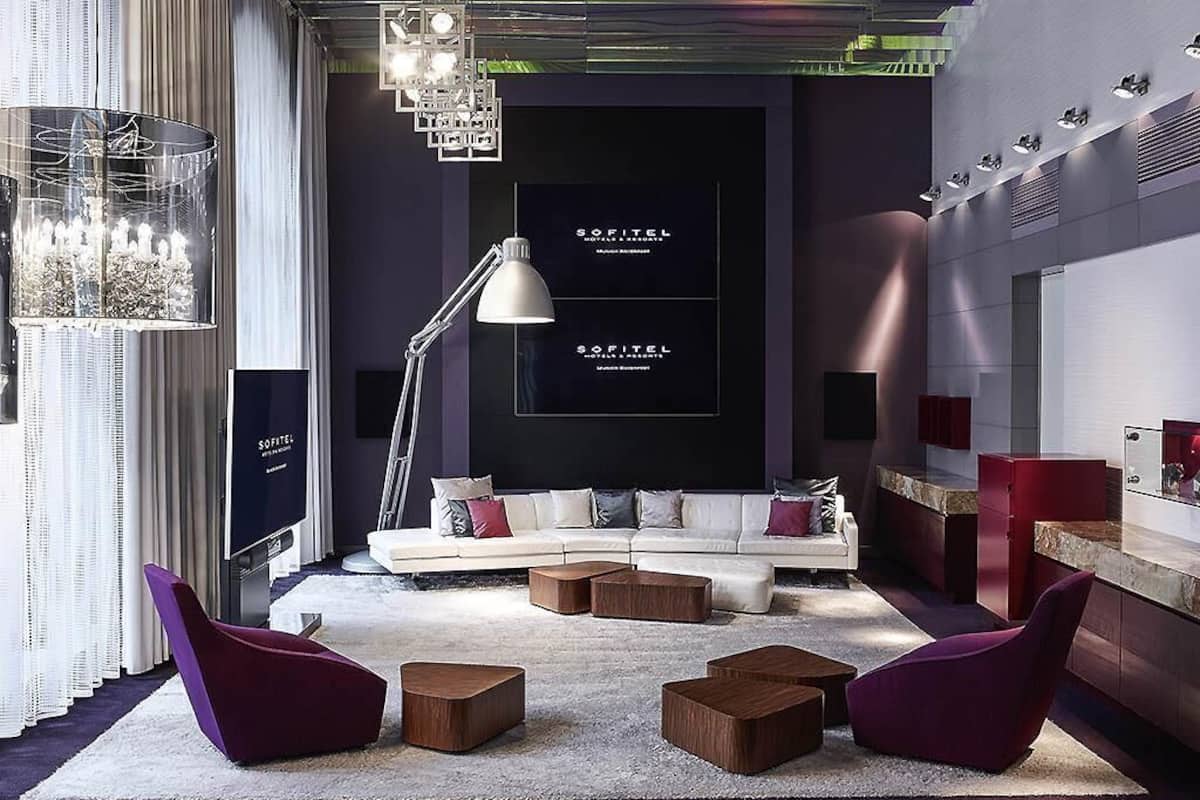 A modern living room with a sofa, two chairs, a coffee table, a TV, and a chandelier.