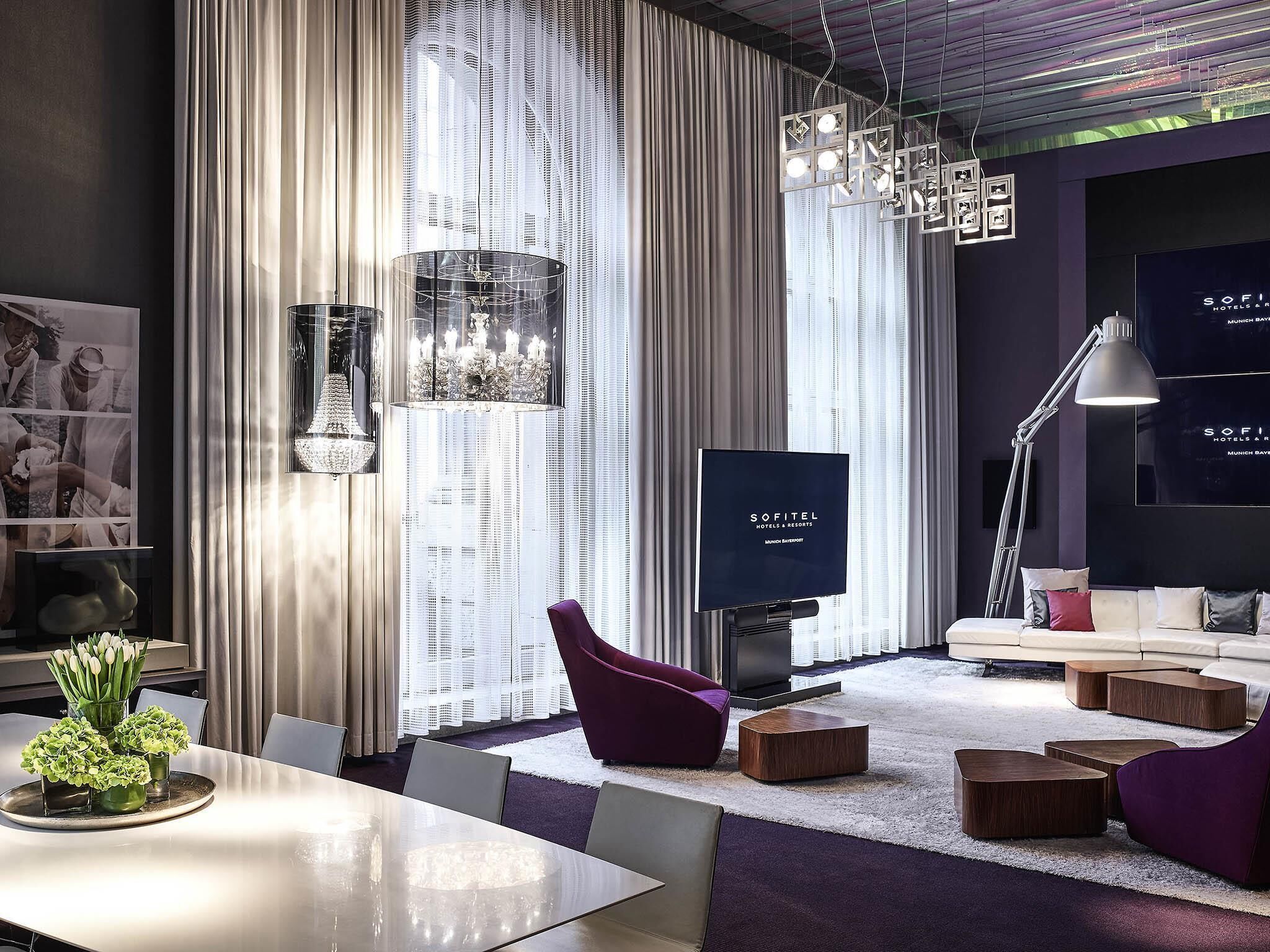 Ein modernes Hotelzimmer mit einem großen Flachbildfernseher, einer Couch, einem Esstisch mit Stühlen und einem dekorativen Kronleuchter.