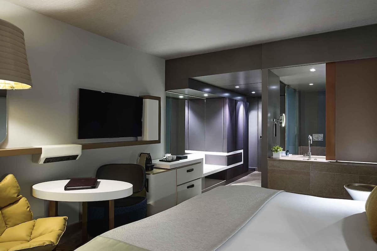 Une chambre d’hôtel équipée d’un lit, d’un bureau, d’une chaise, d’une télévision, d’un miroir et d’une salle de bain.