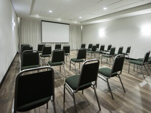 A conference room with rows of green chairs, a white screen, and a wooden floor. - ibis Betim (Betim)