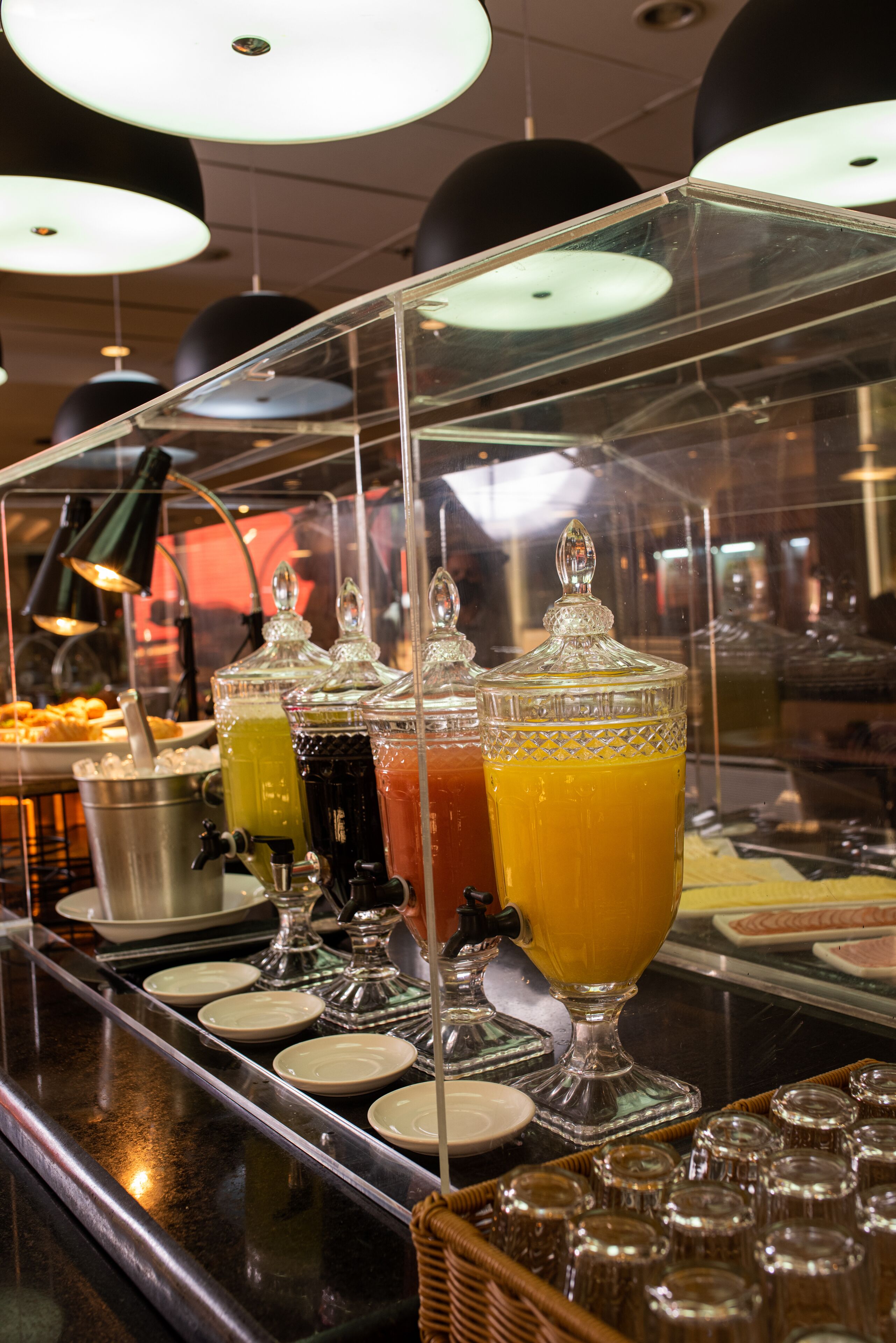 A buffet area with various food and drink options, including a selection of juices and a dish with donuts.