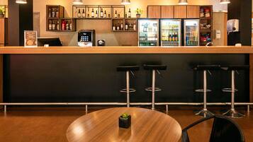 Una zona de bar con mostrador de madera, taburetes, una mesa redonda y estantes con botellas.