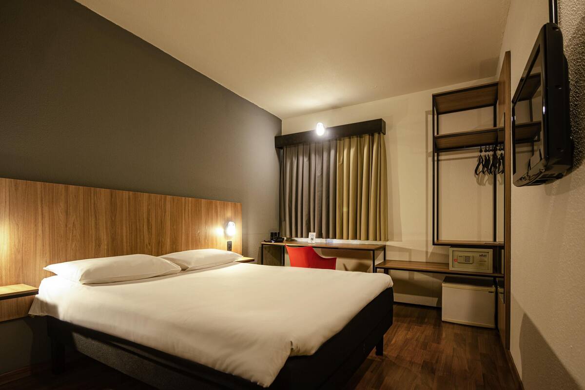 Ein Hotelzimmer mit Bett, Nachttisch, Schreibtisch, Stuhl und Fernseher.