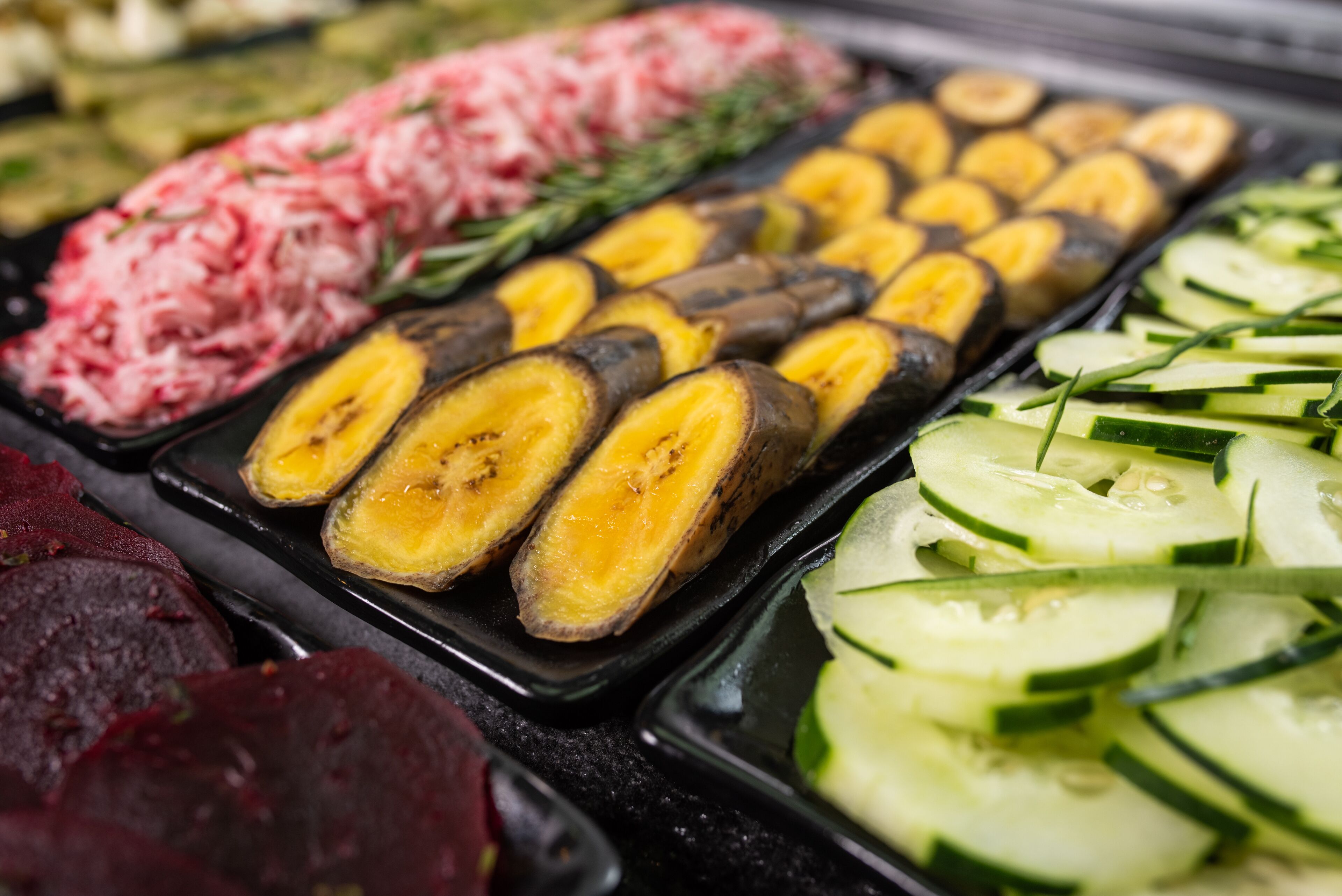 Una variedad de vegetales y frutas cortadas, como pepinos, plátanos y remolachas, dispuestas en una bandeja.
